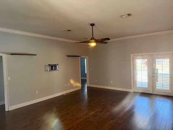 an empty room with wooden floor chandelier fan and windows