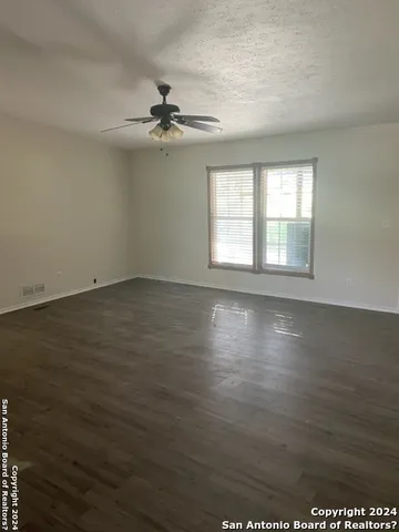 an empty room with wooden floor fan and windows