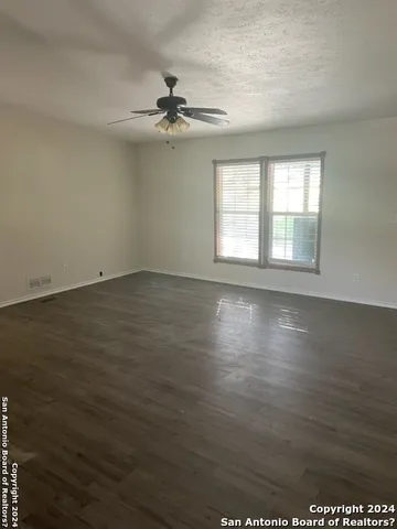 an empty room with wooden floor fan and windows
