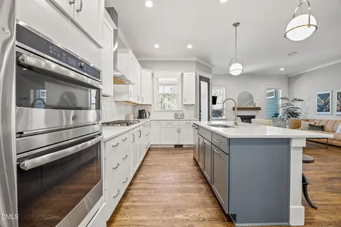 a kitchen with stainless steel appliances granite countertop a white refrigerator a sink dishwasher a stove and white cabinets with wooden floor
