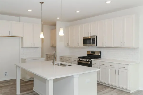a kitchen with stainless steel appliances a stove a sink a microwave a refrigerator white cabinets and wooden floor
