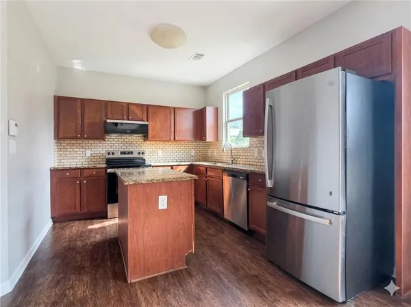 a kitchen with stainless steel appliances granite countertop a refrigerator a sink dishwasher a stove and a microwave oven on the wooden floor