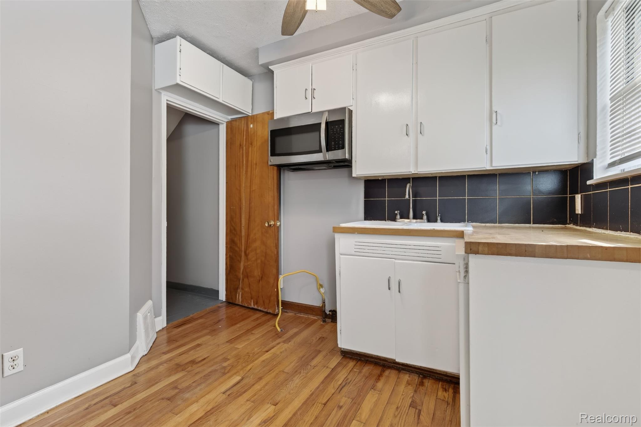 316 Sheffield Avenue Flint, MI 48503 - Photo 11 of 37 Hardwood flooring, white cabinetry, stainless steel microwave, black tile backsplash, and wood-finish countertops