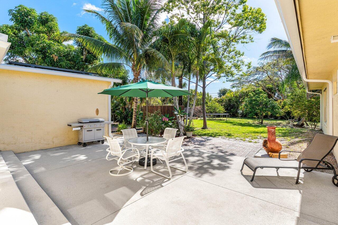 3064 Rostan Lane Palm Springs, FL 33461 - Photo 33 of 49 a view of a patio with a dining table and chairs under an umbrella with large trees