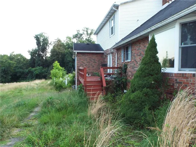 a view of a house with a yard plants and large tree