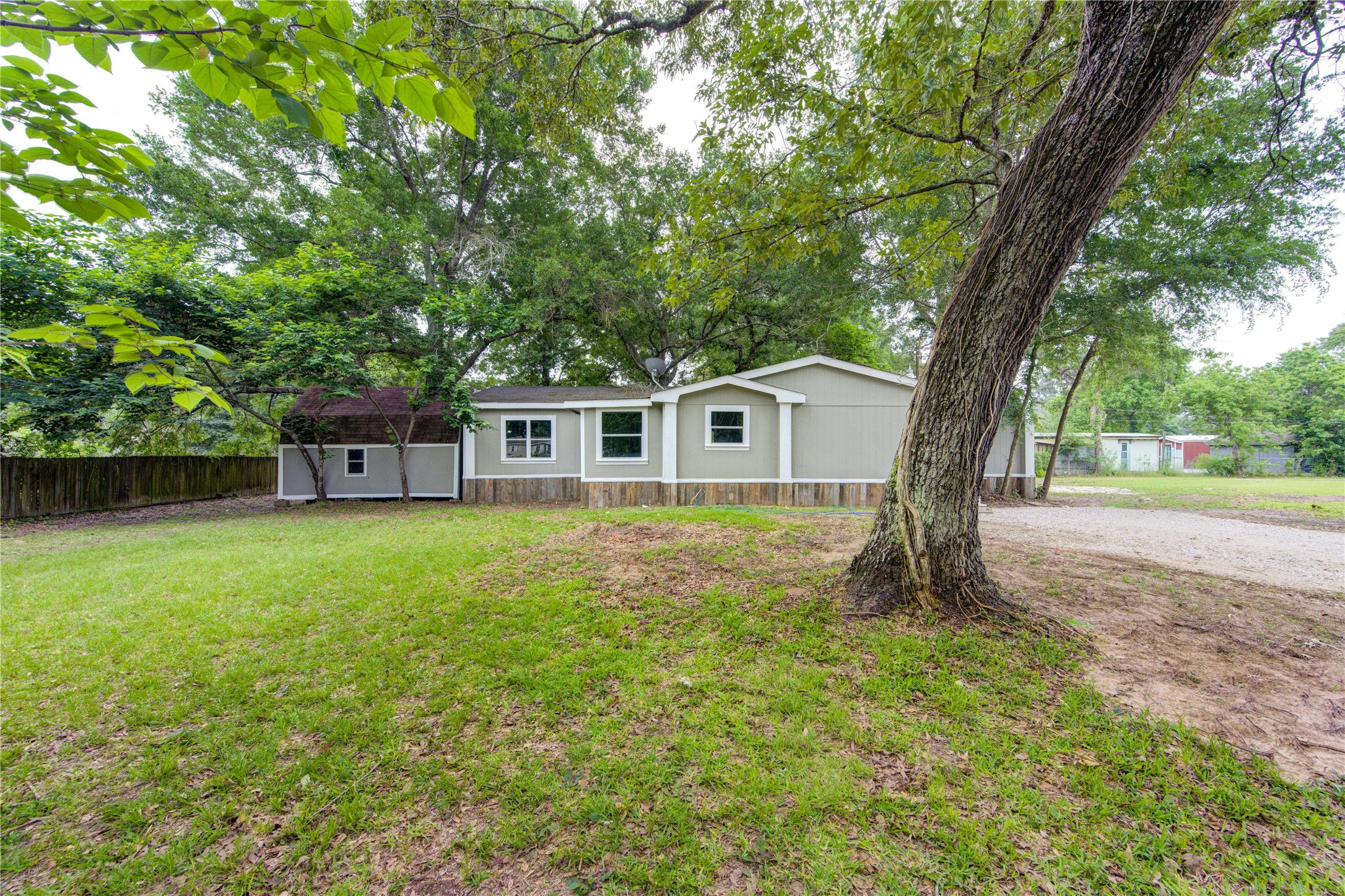 30226 Davis Street Magnolia, TX 77355 - Photo 49 of 50 Charming single-story home with a spacious yard, surrounded by mature trees. Features a gray exterior with white trim, a gravel driveway, and a wooden fence for privacy. Perfect for enjoying outdoor space and tranquility.