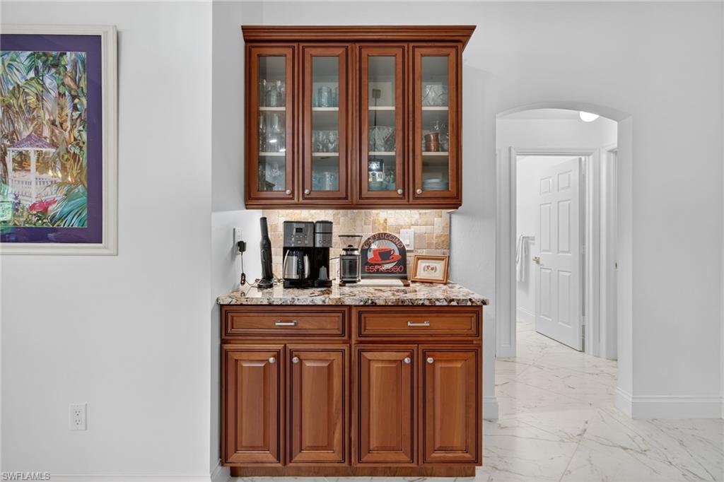 1741 17th Street Southwest Naples, FL 34117 - Photo 14 of 50 Bar area with backsplash, glass insert cabinets, arched walkways, light stone counters, and light satin finish porcelain tile flooring
