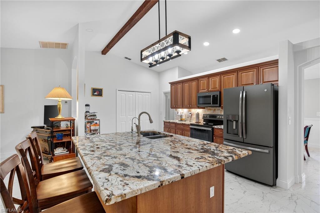 1741 17th Street Southwest Naples, FL 34117 - Photo 15 of 50 Kitchen with stainless steel appliances, light stone countertops, brown cabinets, a kitchen breakfast bar, and decorative backsplash