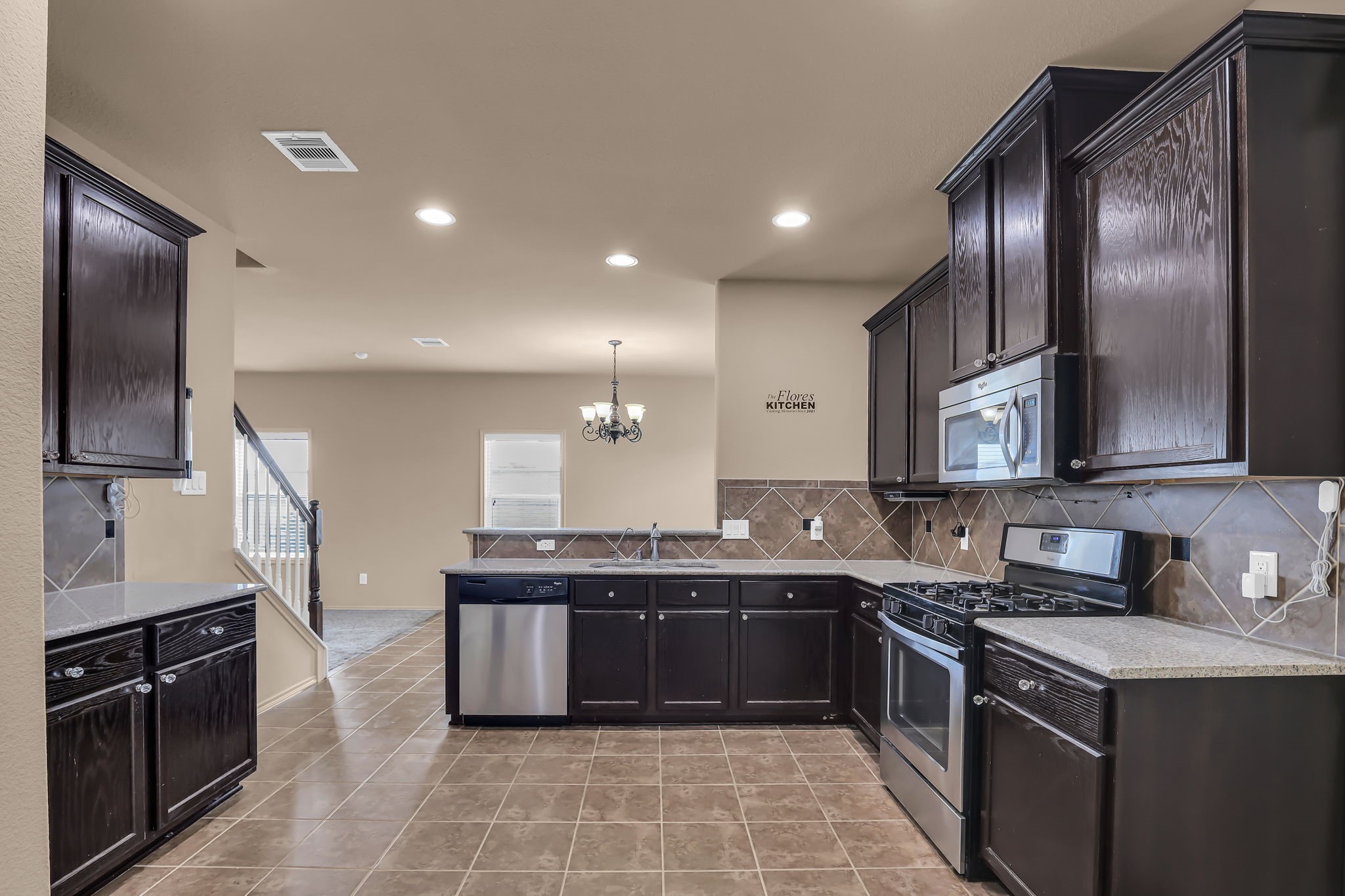 21307 Carleen Creek Trail Spring, TX 77379 - Photo 7 of 25 Open concept kitchen with dark wood cabinets, stainless steel appliances, and tiled flooring. It features a spacious layout with a view into the adjacent dining area, complete with recessed lighting and a chandelier.