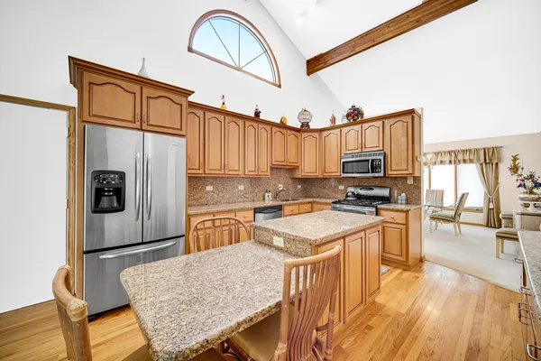 a kitchen with stainless steel appliances granite countertop a stove top oven a sink a dining table and chairs with wooden floor