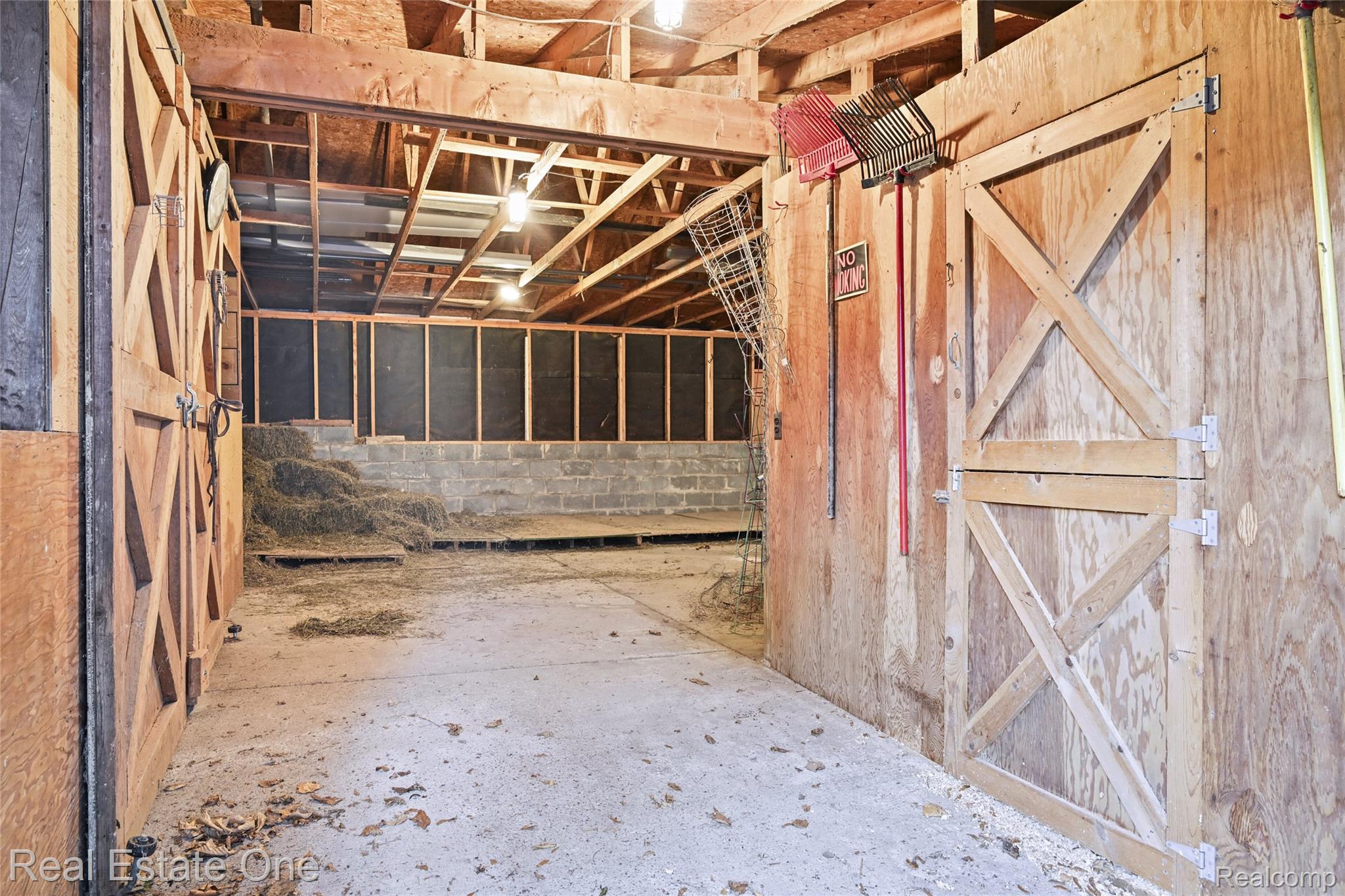 895 Rowe Road Milford, MI 48380 - Photo 24 of 50 Barn 1 Interior barn featuring wood-paneled walls, exposed ceiling trusses, concrete flooring, and stall doors with crossbuck detailing