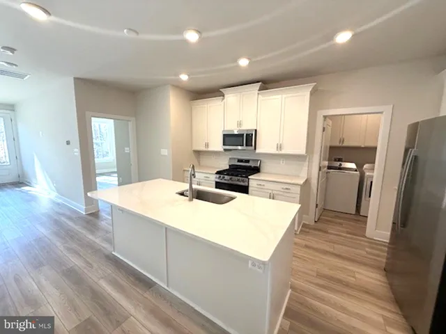 a large kitchen with stainless steel appliances kitchen island a sink dishwasher a refrigerator and a stove with wooden floor