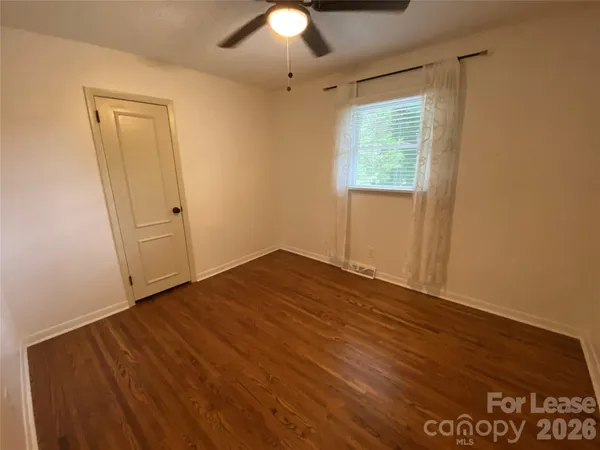 an empty room with wooden floor chandelier fan and windows