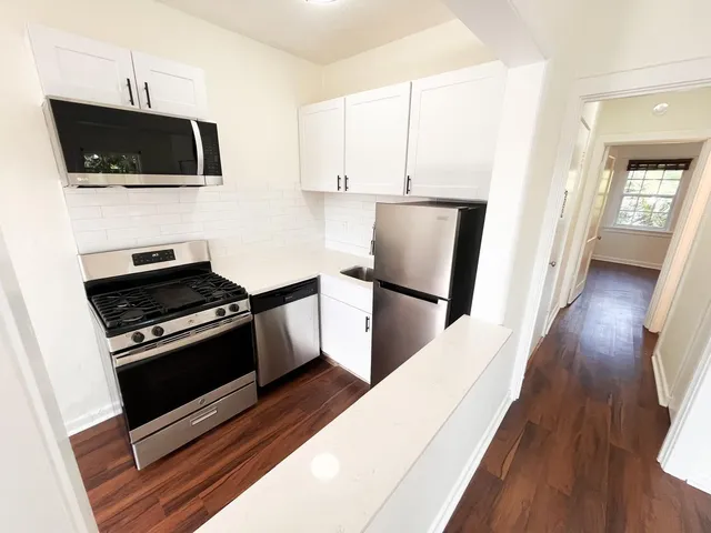 a kitchen with stainless steel appliances a stove a microwave a sink a refrigerator white cabinets and wooden floor