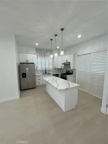 a large white kitchen with stainless steel appliances kitchen island a large counter top a stove a sink and a refrigerator