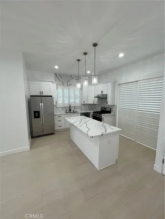 a large white kitchen with stainless steel appliances kitchen island a large counter top a stove a sink and a refrigerator