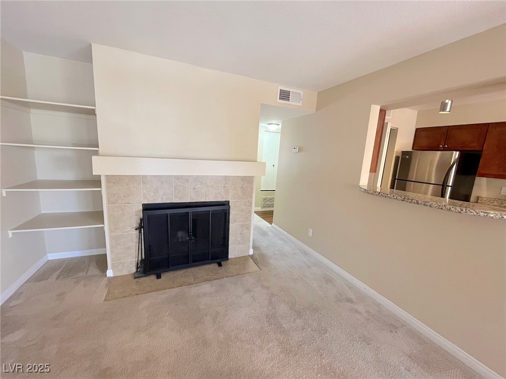 2750 South Durango Drive, Unit 2139 Las Vegas, NV 89117 - Photo 2 of 21 Unfurnished living room featuring a tiled fireplace and light carpet