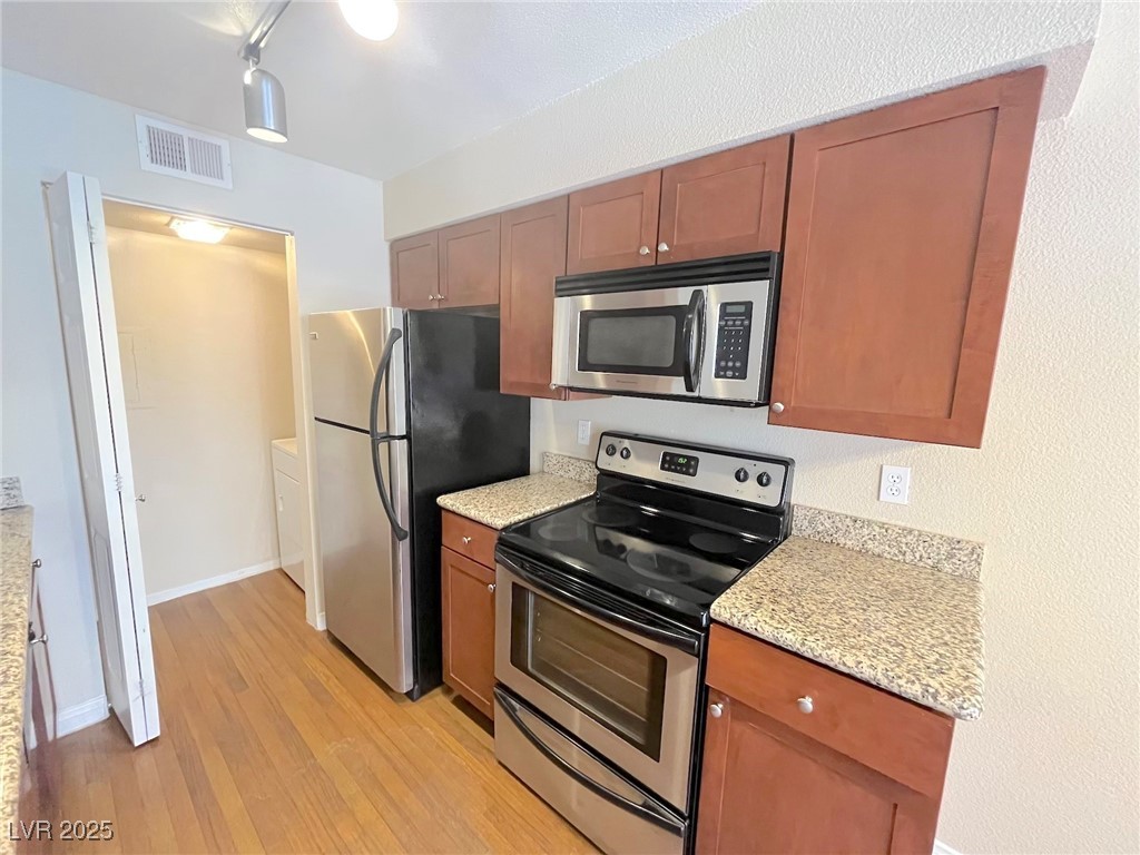 2750 South Durango Drive, Unit 2139 Las Vegas, NV 89117 - Photo 9 of 21 Kitchen featuring stainless steel appliances, light wood finished floors, light stone countertops, and brown cabinets