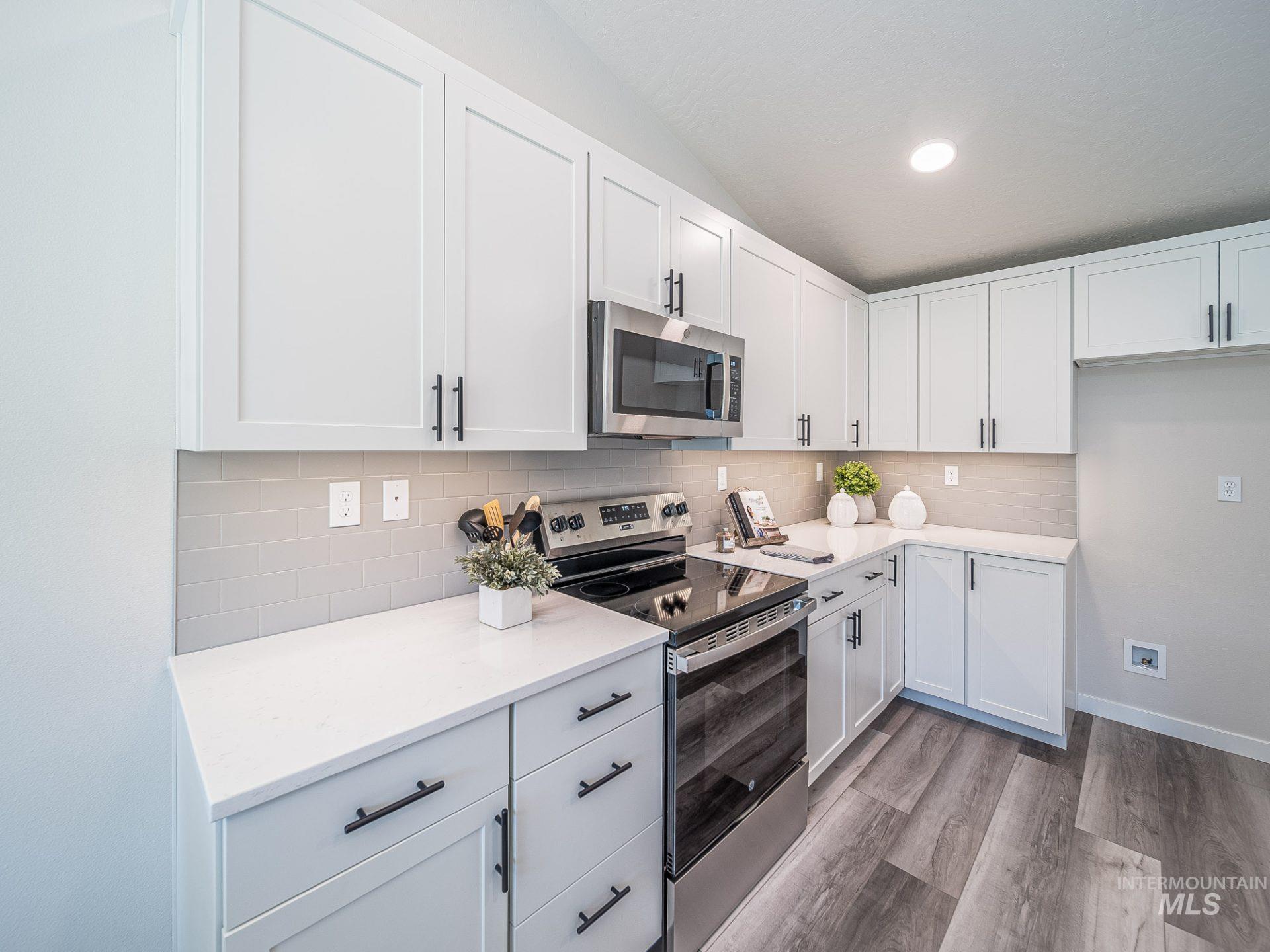 3291 East Fitz Roy Street Kuna, ID 83634 - Photo 2 of 9 Kitchen with appliances with stainless steel finishes, decorative backsplash, white cabinetry, light wood-style floors, and light stone counters