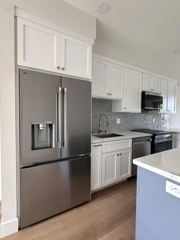 a kitchen with stainless steel appliances granite countertop a refrigerator a stove a sink and white cabinets