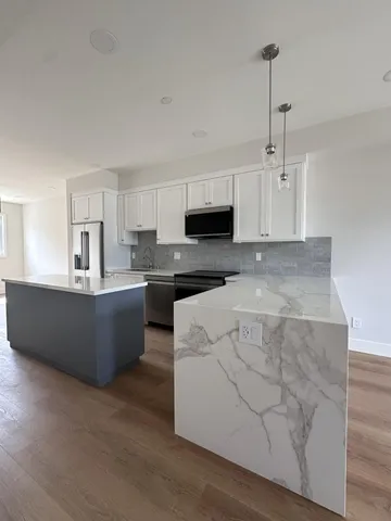 a large kitchen with stainless steel appliances granite countertop a stove a sink a refrigerator a microwave oven and white cabinets with wooden floor