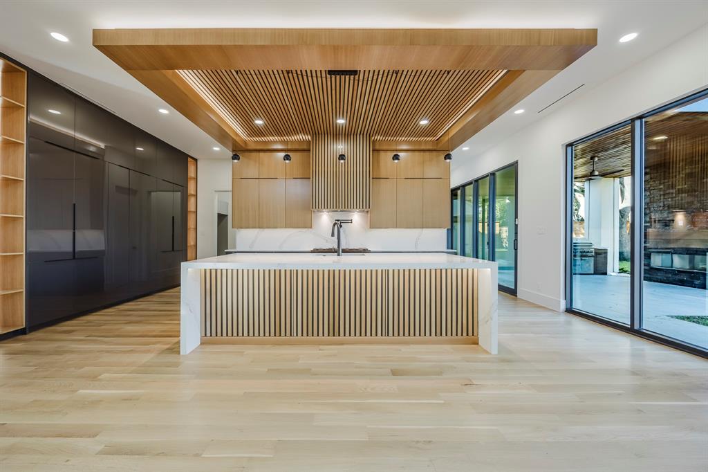 Kitchen featuring modern cabinets, a large island with sink, light stone counters, light brown cabinets, and a kitchen bar