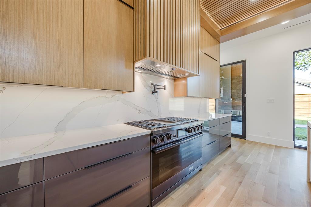 5723 Meletio Lane Dallas, TX 75230 - Photo 13 of 38 Kitchen with modern cabinets, light stone countertops, black gas stove, premium range hood, and light wood-style flooring