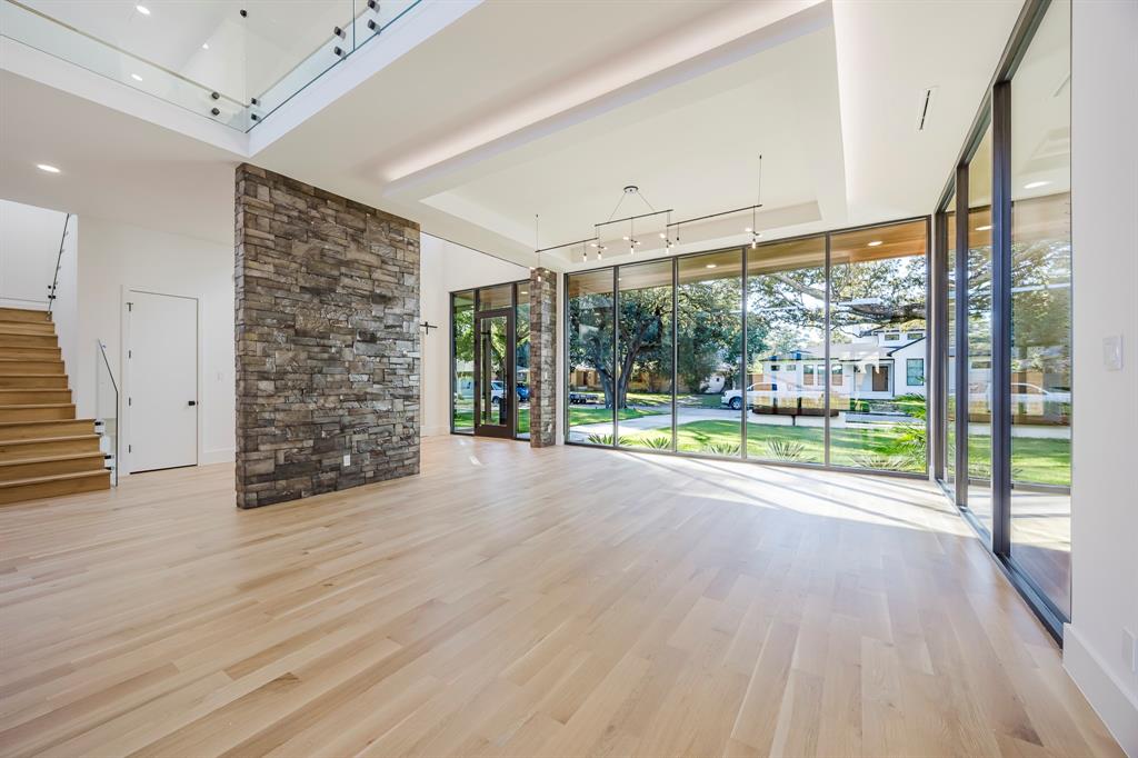 5723 Meletio Lane Dallas, TX 75230 - Photo 10 of 38 Unfurnished living room with a wall of windows, light wood-style flooring, a tray ceiling, and stairway