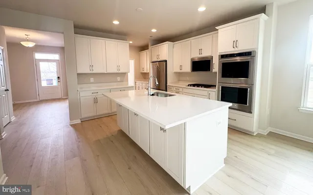 a kitchen with stainless steel appliances a stove top oven a sink a refrigerator white cabinets and wooden floor