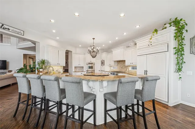 a kitchen with stainless steel appliances kitchen island granite countertop a stove top oven a refrigerator a sink and dishwasher with wooden floor