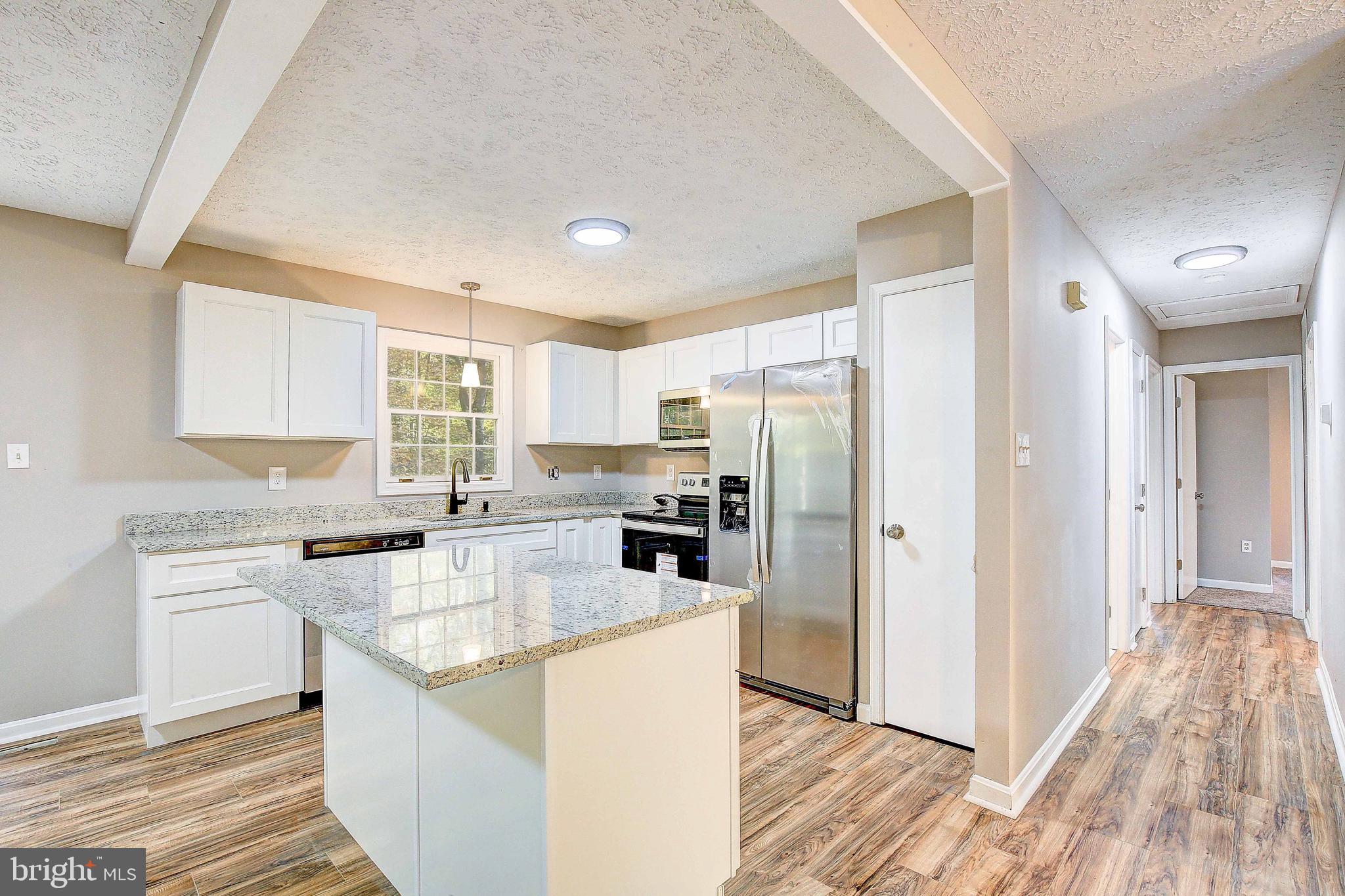 a kitchen with stainless steel appliances kitchen island granite countertop a refrigerator a sink dishwasher a stove with wooden cabinets and floor