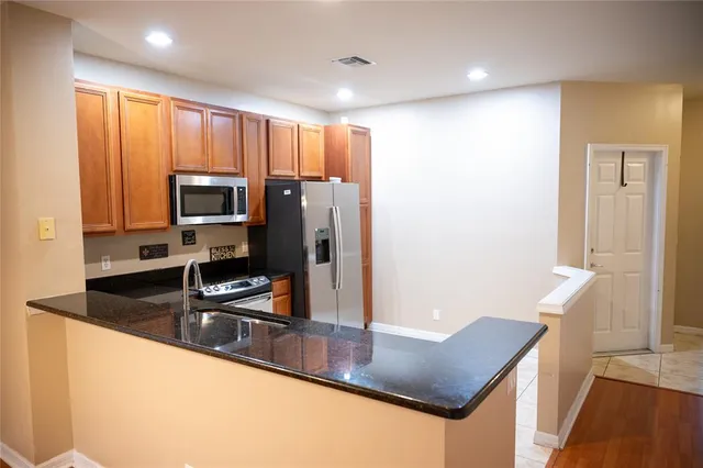 a kitchen with stainless steel appliances granite countertop a refrigerator a stove and a sink with wooden floor