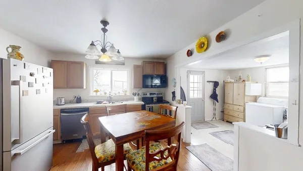 a kitchen with stainless steel appliances granite countertop a refrigerator a sink dishwasher a dining table and chairs with wooden floor