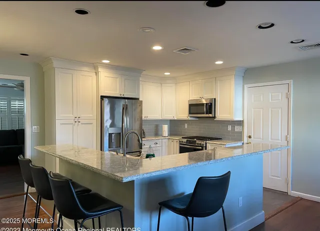 a kitchen with stainless steel appliances granite countertop a sink a stove a refrigerator cabinets and chairs