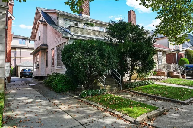 a view of a brick house with a yard plants and large tree