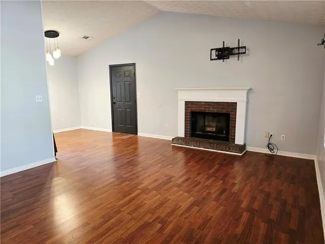 an empty room with wooden floor fireplace and windows