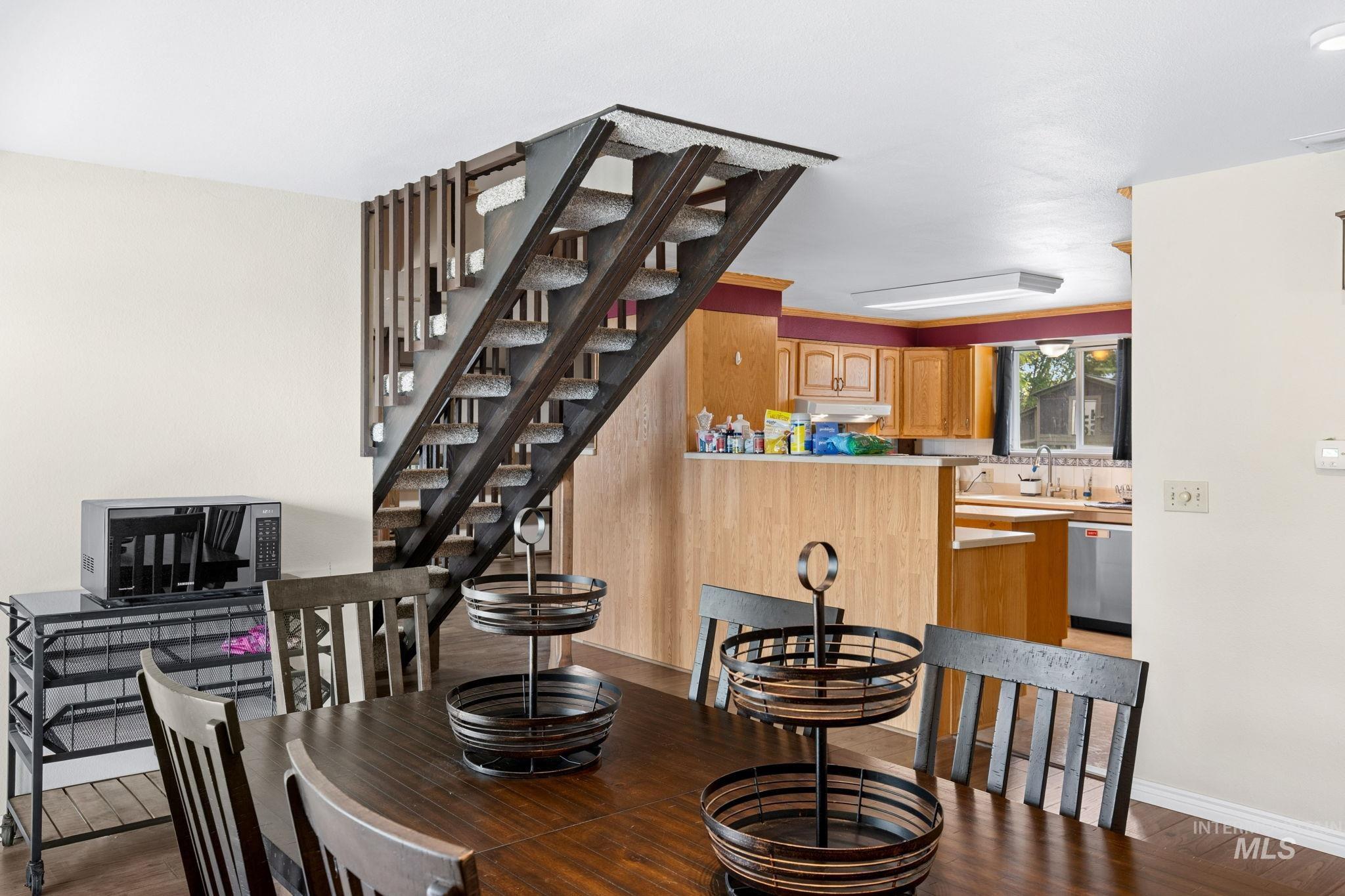 18338 Pride Lane Caldwell, ID 83607 - Photo 10 of 50 Dining area featuring wood-finish flooring, a contemporary open staircase with wood railings, and a partial view of the kitchen with wood cabinetry and a window