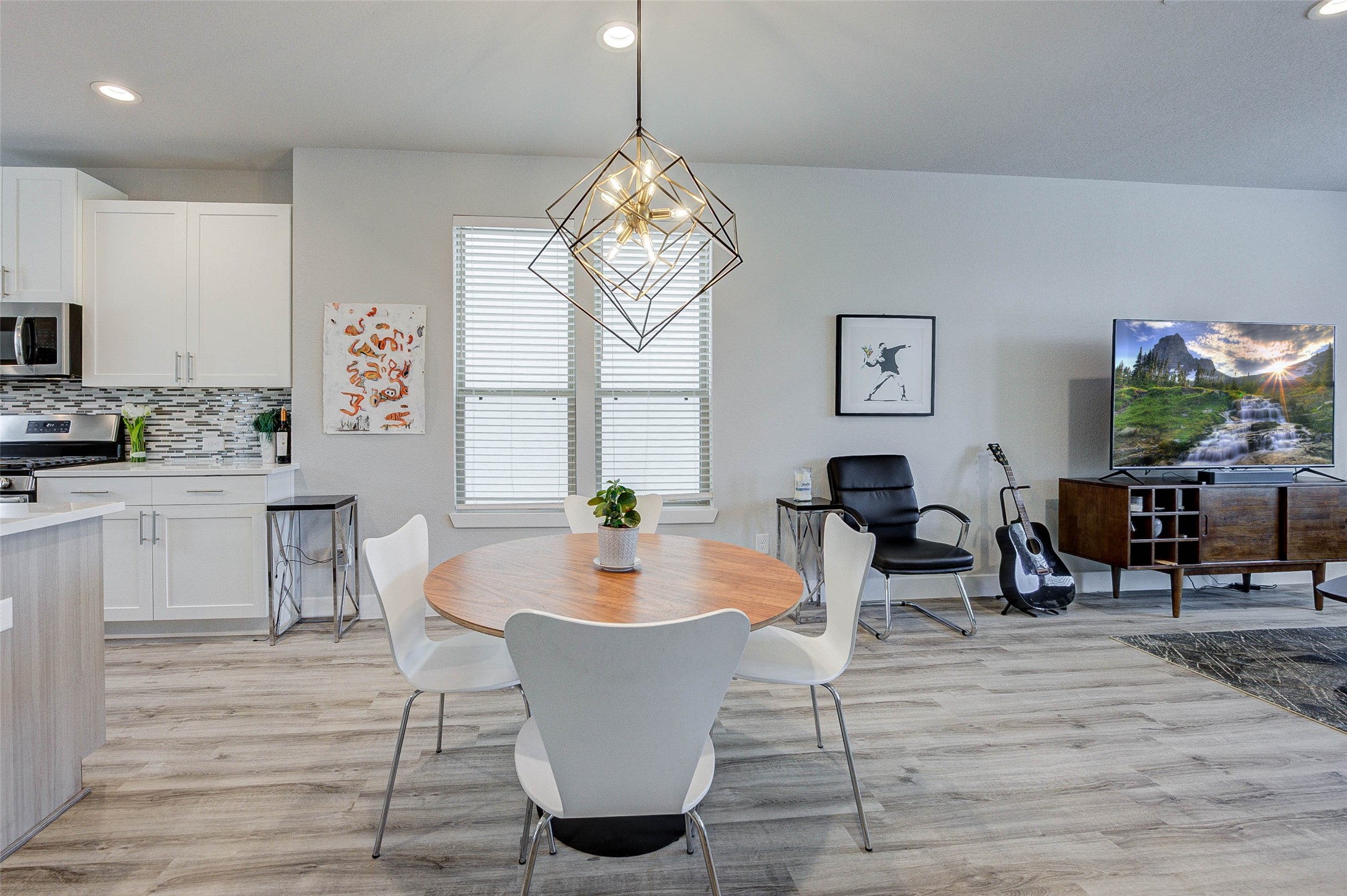 18732 Centro Main Street, Unit B Shenandoah, TX 77385 - Photo 13 of 42 This modern open-plan living area features a sleek kitchen with stainless steel appliances and white cabinetry. It seamlessly flows into a cozy dining space with a stylish geometric light fixture. The living area includes a comfortable chair, TV setup, and contemporary decor, all set on elegant wood flooring.