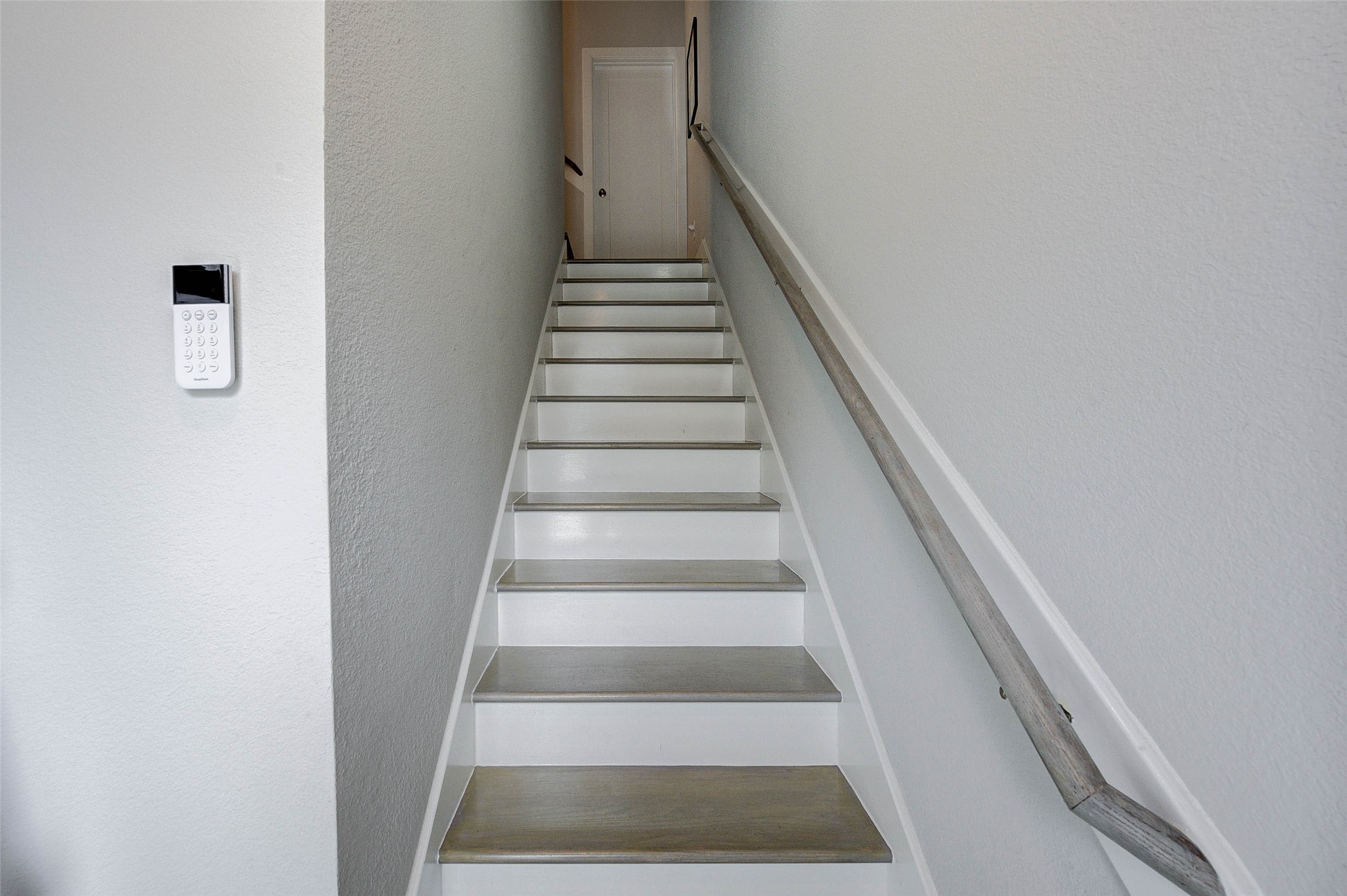 18732 Centro Main Street, Unit B Shenandoah, TX 77385 - Photo 14 of 42 This photo shows a narrow staircase with a wooden handrail leading to a door at the top. The walls are painted white, and a security keypad is mounted on the side wall.