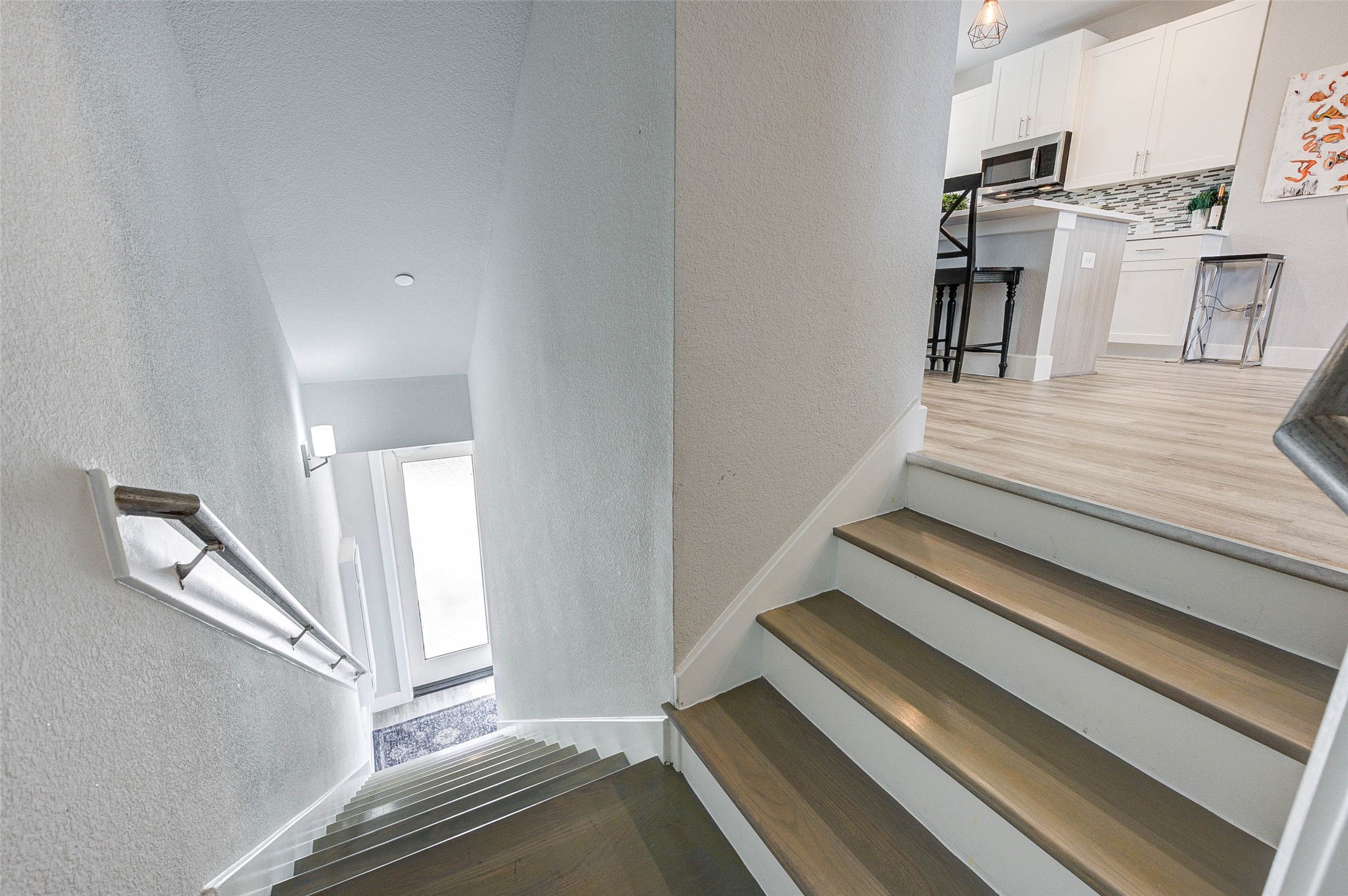 18732 Centro Main Street, Unit B Shenandoah, TX 77385 - Photo 15 of 42 This photo shows a staircase leading to a bright, modern kitchen area with light wood flooring, white cabinetry, and a decorative backsplash. The space is open and inviting, with contemporary design elements.
