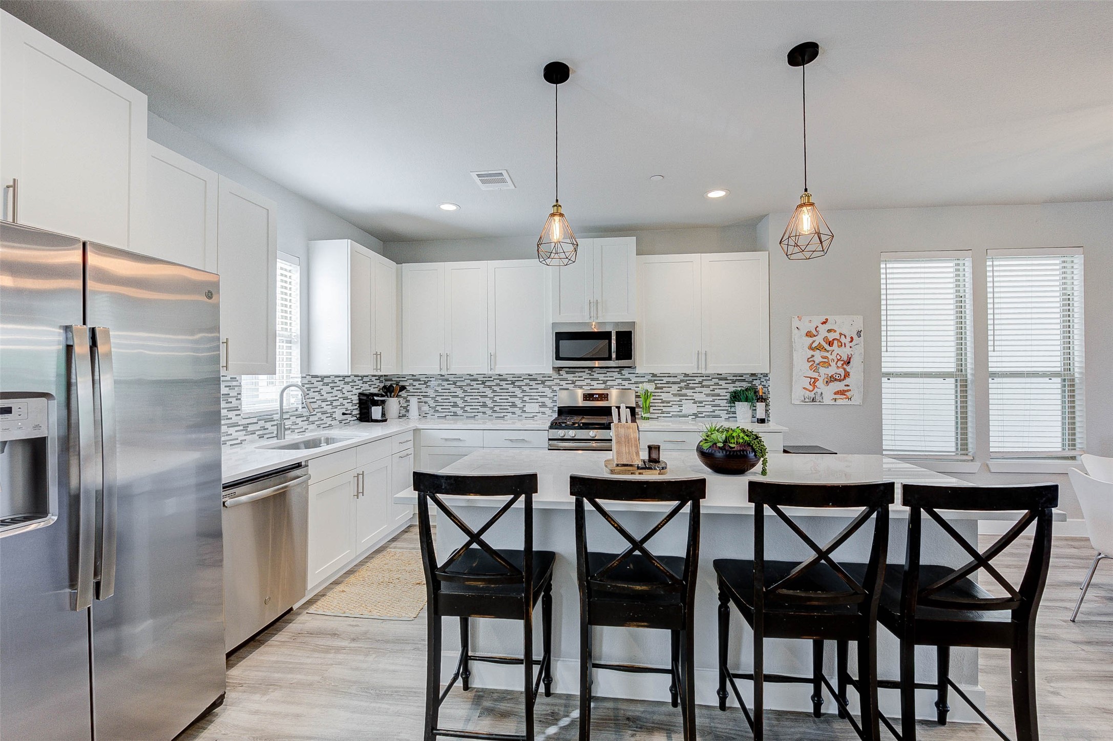 18732 Centro Main Street, Unit B Shenandoah, TX 77385 - Photo 22 of 42 Modern kitchen with sleek white cabinetry, stainless steel appliances, and a stylish backsplash. The island features seating for four and contemporary pendant lighting. Spacious and bright with plenty of windows.