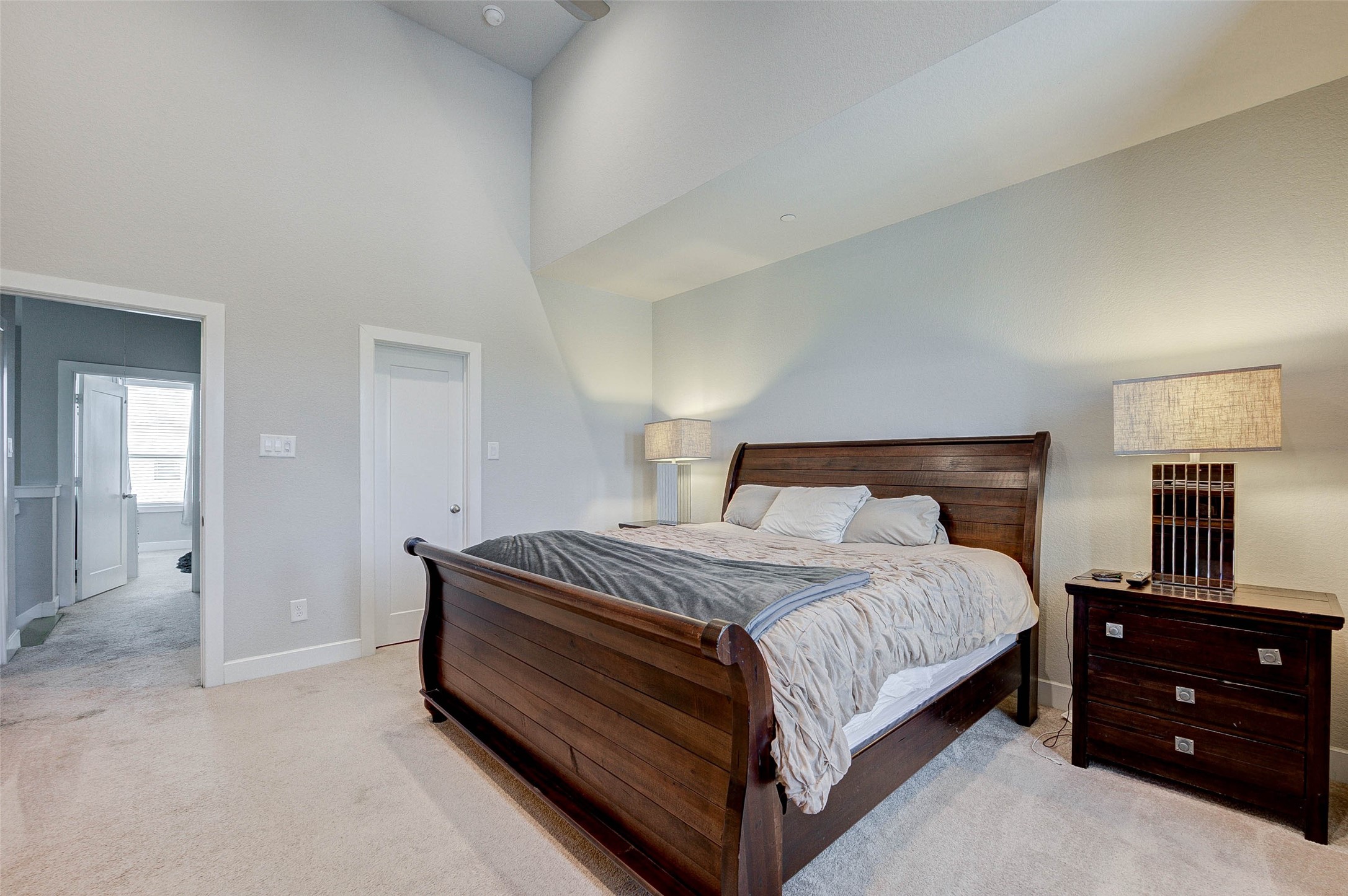18732 Centro Main Street, Unit B Shenandoah, TX 77385 - Photo 30 of 42 This spacious bedroom features a high ceiling and soft carpeting, creating an inviting atmosphere. It includes a large wooden bed with matching nightstands and modern lamps, offering a comfortable and stylish retreat. A doorway leads to additional living spaces, enhancing the room's functionality.