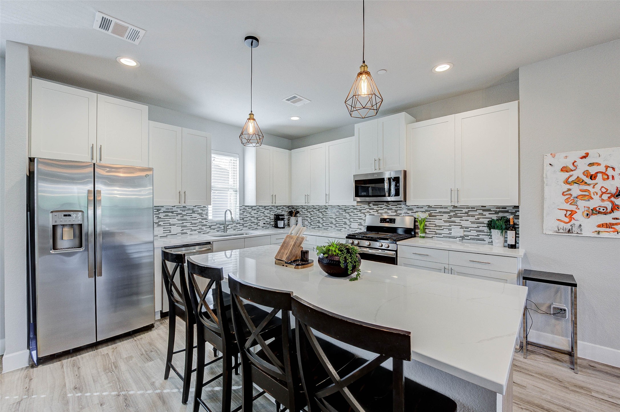 18732 Centro Main Street, Unit B Shenandoah, TX 77385 - Photo 3 of 42 This modern kitchen features sleek white cabinetry, stainless steel appliances, and a stylish tile backsplash. The spacious island with pendant lighting offers additional seating and prep space, perfect for entertaining.