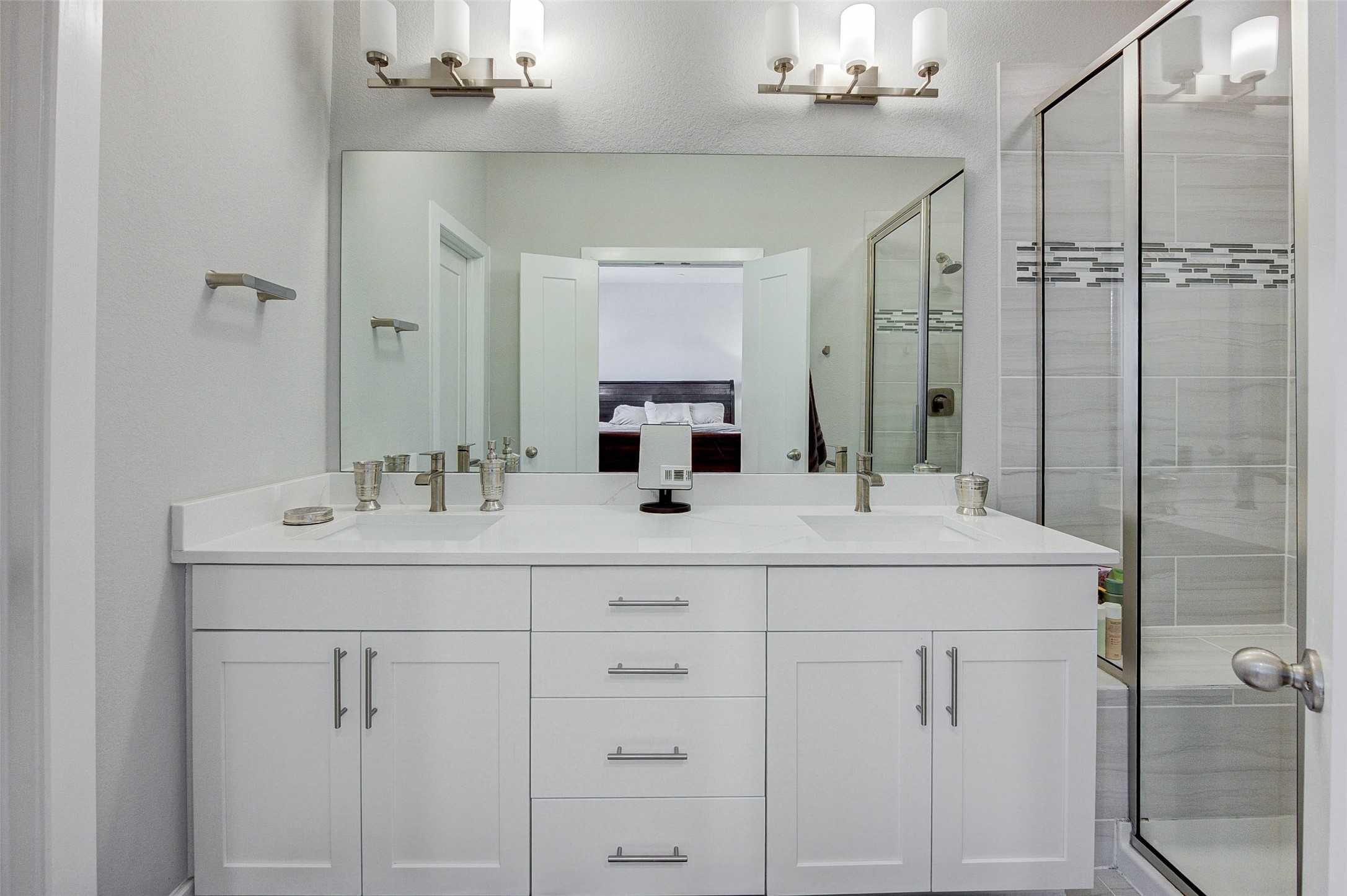 18732 Centro Main Street, Unit B Shenandoah, TX 77385 - Photo 32 of 42 This modern bathroom features a spacious double vanity with sleek white cabinetry and dual sinks. It includes a large mirror and elegant lighting fixtures, with a glass-enclosed shower showcasing stylish tile work.