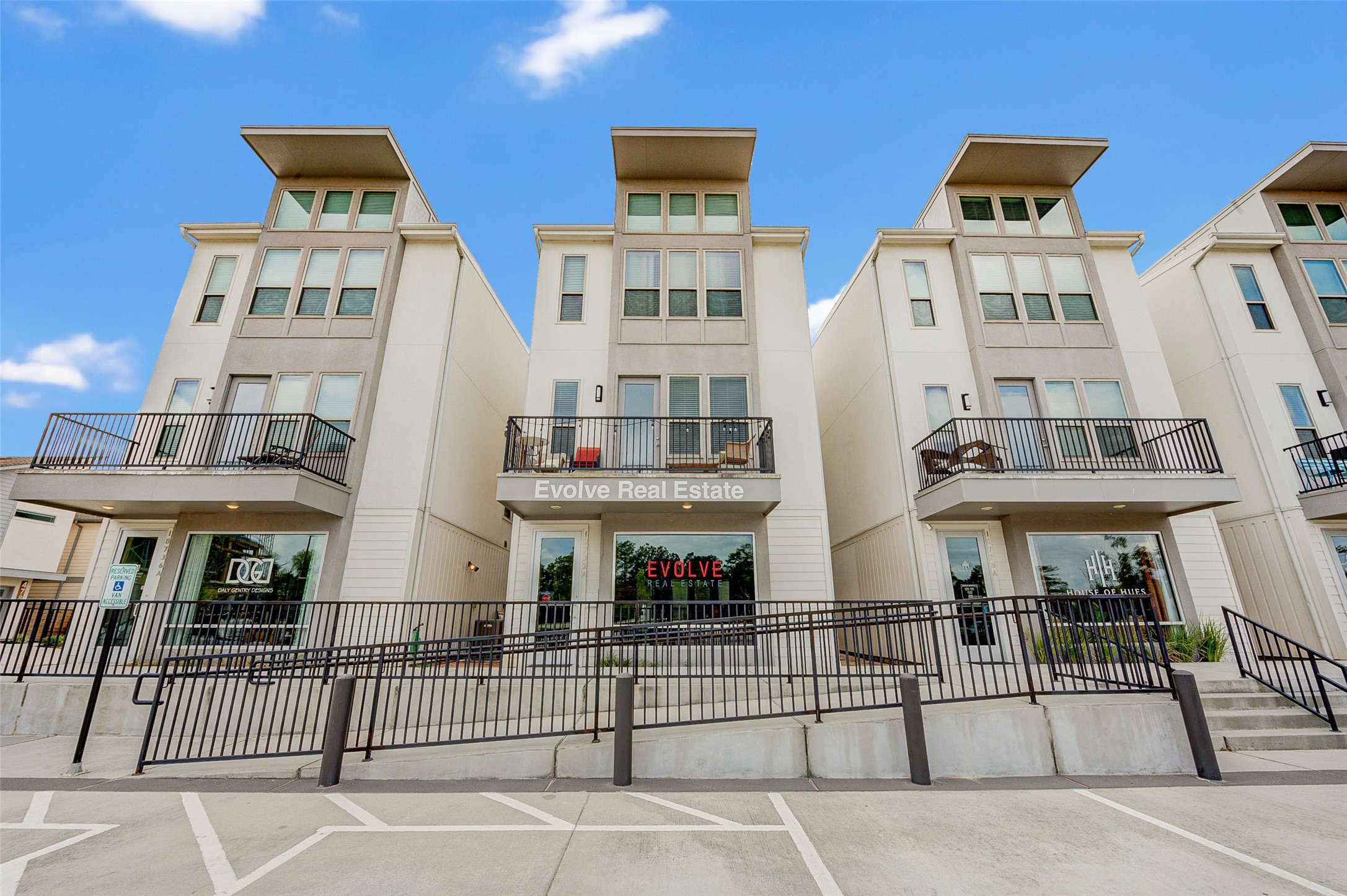 18732 Centro Main Street, Unit B Shenandoah, TX 77385 - Photo 4 of 42 Modern multi-story townhouses with large windows and private balconies, featuring a central real estate office. The building has a clean, contemporary design with a welcoming entrance and ample parking space.