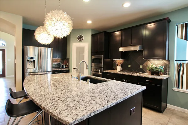 a kitchen with stainless steel appliances kitchen island granite countertop a table chairs and a refrigerator