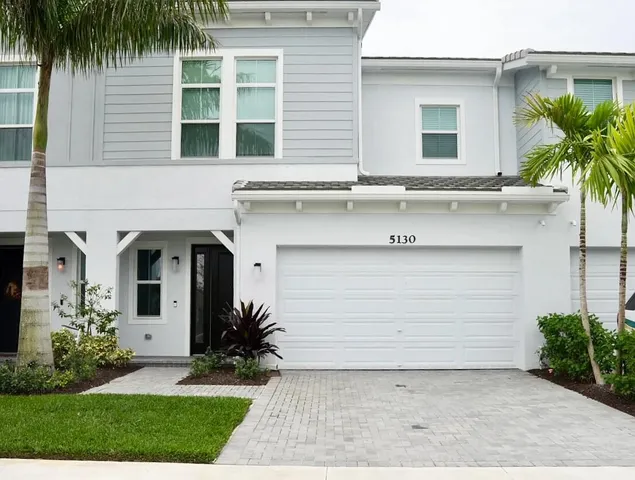 a front view of a house with a garden and palm trees