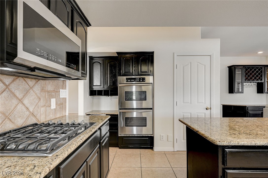2955 El Camino Road Las Vegas, NV 89146 - Photo 6 of 99 Kitchen featuring dark cabinetry, stainless steel appliances, tasteful backsplash, and light stone countertops