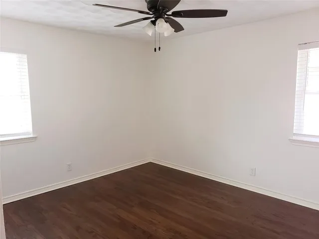 an empty room with wooden floor a ceiling fan and windows