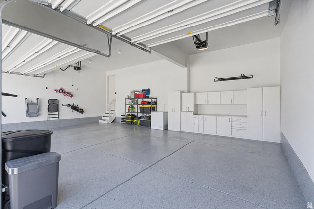7685 Timber Country Road Eagle Mountain, UT 84005 - Photo 27 of 39 Spacious garage featuring an epoxy-coated floor, extensive built-in white cabinetry, integrated overhead fluorescent lighting, and a staircase